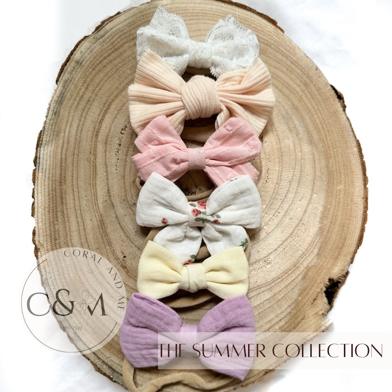 May include: A set of six hair bows in various colors and patterns, including pink, white, yellow, and floral print. The bows are arranged on a wooden surface and are part of a collection called "The Summer Collection".