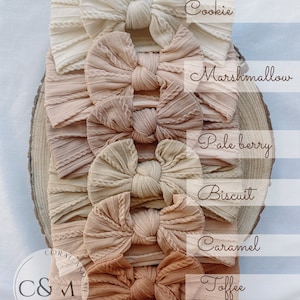 K&ouml;nnte beinhalten: Sechs verschiedene Farben von gestrickten Stirnb&auml;ndern mit Schleifen. Die Farben sind Cookie, Marshmallow, Pale Berry, Biscuit, Caramel und Toffee.