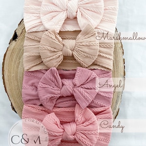 K&ouml;nnte beinhalten: Vier rosa, pfirsichfarbene und korallenfarbene gekn&uuml;pfte Stirnb&auml;nder mit Schleifen. Die Stirnb&auml;nder sind &uuml;bereinander gestapelt. Das oberste Stirnband ist mit "Candyfloss" beschriftet, das zweite Stirnband mit "Marshmallow", das dritte Stirnband mit "Angel" und das unterste Stirnband mit "Candy".