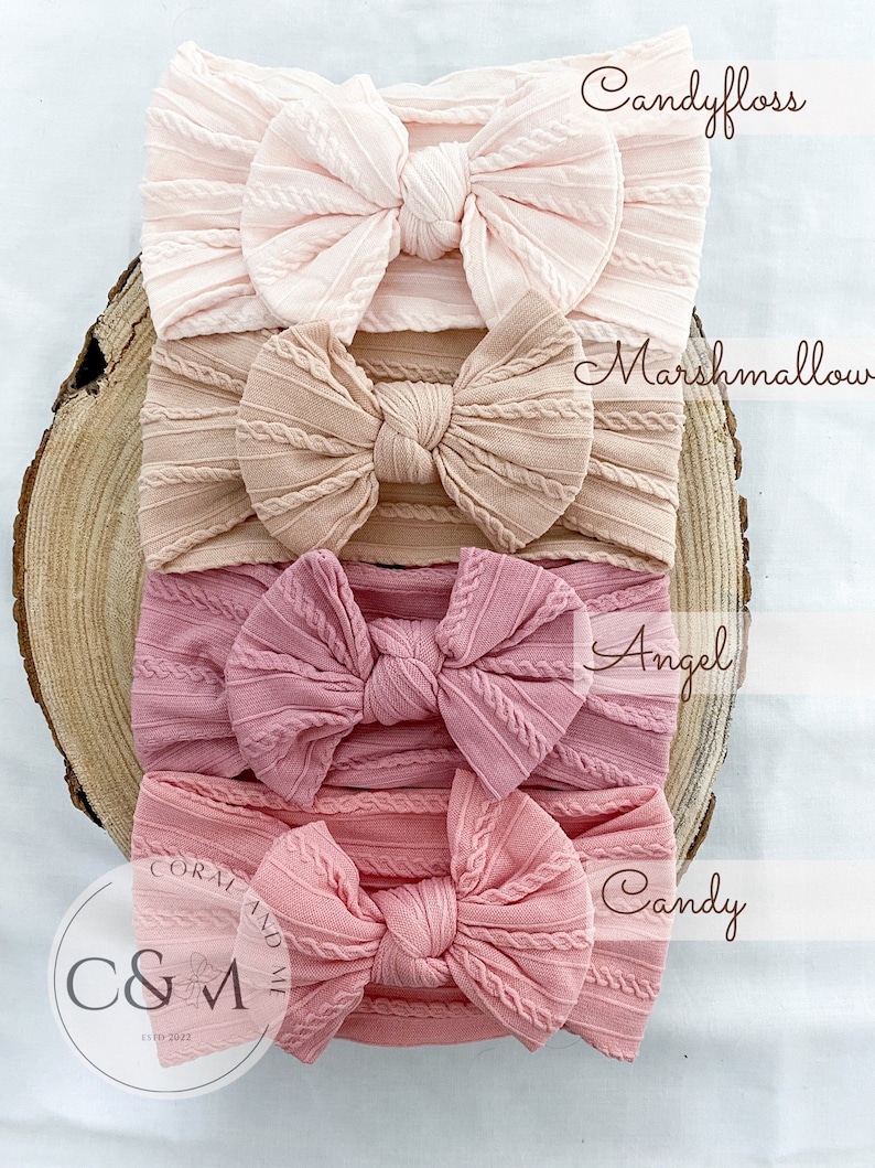K&ouml;nnte beinhalten: Vier rosa, pfirsichfarbene und korallenfarbene gekn&uuml;pfte Stirnb&auml;nder mit Schleifen. Die Stirnb&auml;nder sind &uuml;bereinander gestapelt. Das oberste Stirnband ist mit "Candyfloss" beschriftet, das zweite Stirnband mit "Marshmallow", das dritte Stirnband mit "Angel" und das unterste Stirnband mit "Candy".