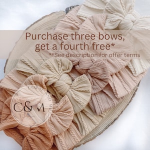 May include: Five beige and brown fabric hair bows with a cable knit texture. The bows are arranged in a circle on a wooden surface. The text "Purchase three bows, get a fourth free*" is displayed above the bows. The text "**See description for offer terms" is displayed below the bows.