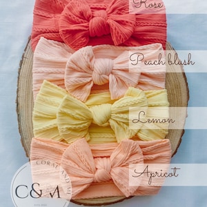 K&ouml;nnte beinhalten: Vier verschiedene Farben von gekn&uuml;pften Stirnb&auml;ndern, von oben nach unten: Rose, Pfirsichbl&uuml;te, Zitrone und Aprikose. Die Stirnb&auml;nder sind auf einer Holzoberfl&auml;che angeordnet. Der Text "Coral and Me" ist in der linken unteren Ecke des Bildes sichtbar.
