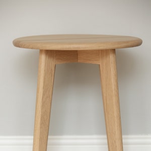 May include: A round wooden side table with a light wood finish and three legs. The table is on a beige carpet.