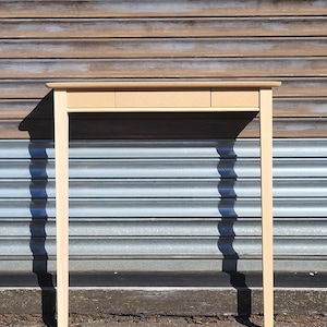 May include: A light-colored wooden console table featuring a rectangular top and four straight, slender legs. The front of the table includes a horizontal panel with three distinct sections, suggesting the presence of drawers or storage compartments.