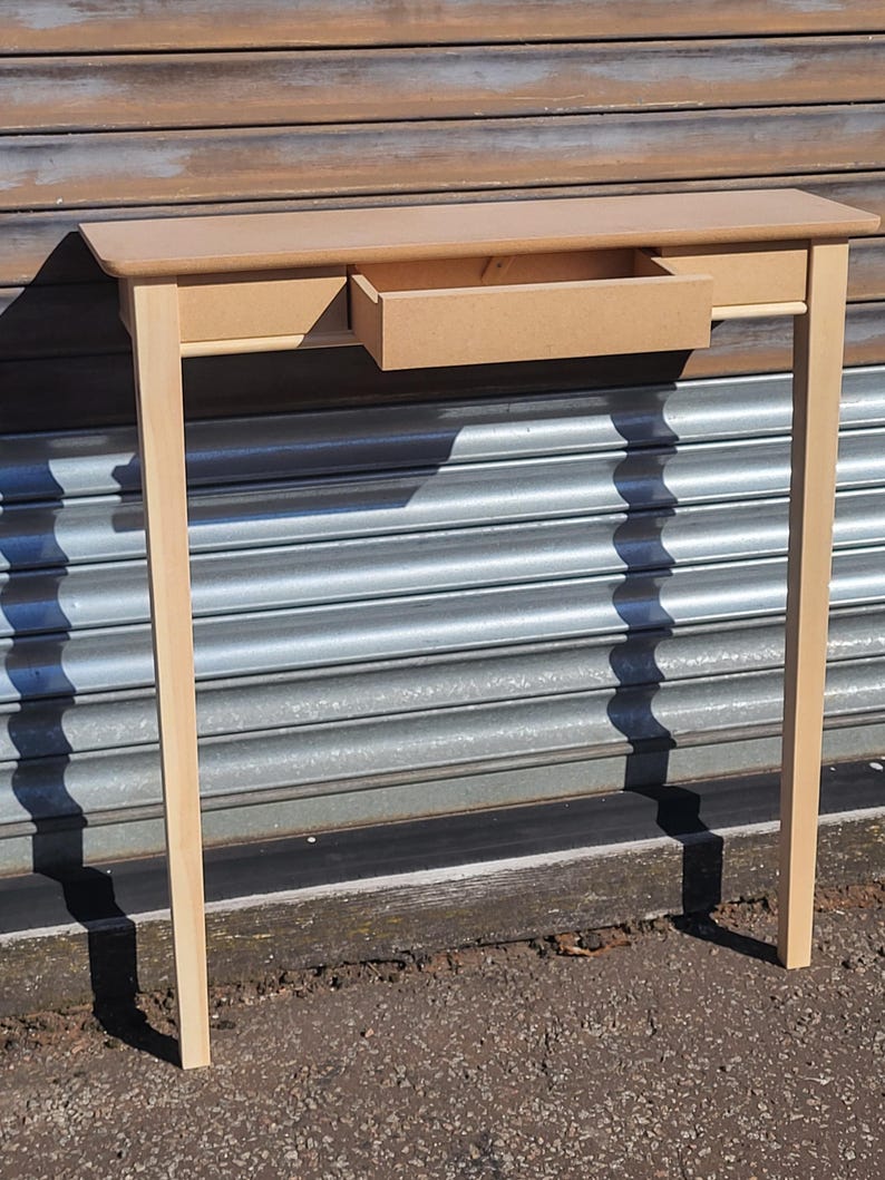 May include: A light tan wooden console table featuring a rectangular top and four straight legs. The table includes a single central drawer that is partially pulled out, revealing the interior compartment and the smooth, unfinished wood surface.