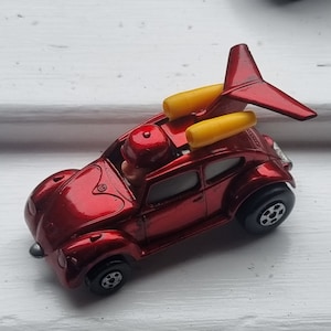 May include: A red toy car with a jet engine fixed to the roof. The car has black wheels and a small figure in the driver's seat. The jet engine has yellow cylinders and a red wing.
