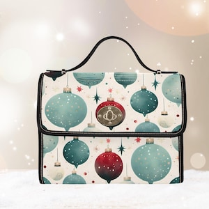 以下が含まれることがあります： 黒いハンドルとトリムが付いた長方形のハンドバッグ。バッグは、クリーム色の背景に、ティールと赤のクリスマスオーナメントの繰り返し模様が特徴です。オーナメントは白いドットと星で飾られています。