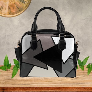 May include: Black, white, and gray geometric pattern handbag with black handles and a shoulder strap. The bag has a structured shape and gold-colored hardware. The design features a modern, abstract pattern.