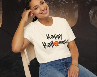 May include: A cream-colored short-sleeve t-shirt featuring the text Happy Halloween in a black dripping font. The design includes a small orange jack-o'-lantern replacing the letter O, along with tiny spider and web graphics.