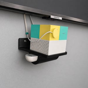 May include: A multi-colored, geometric speaker system with teal, yellow, and white blocks, mounted on a black shelf. A white Bose device sits below. The system is connected to a Samsung TV.