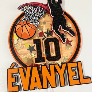 May include: A basketball-themed cake topper featuring a basketball, hoop, and a player shooting a basket. The topper also includes the number 10 and the name "EVANYEL" in orange and black.