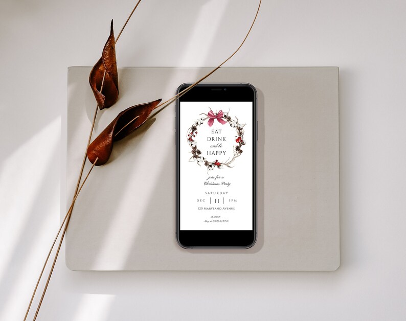 May include: A smartphone displaying a digital Christmas party invitation with a watercolor wreath and the text "Eat Drink and be Happy". The invitation includes the date, time, and location of the party.
