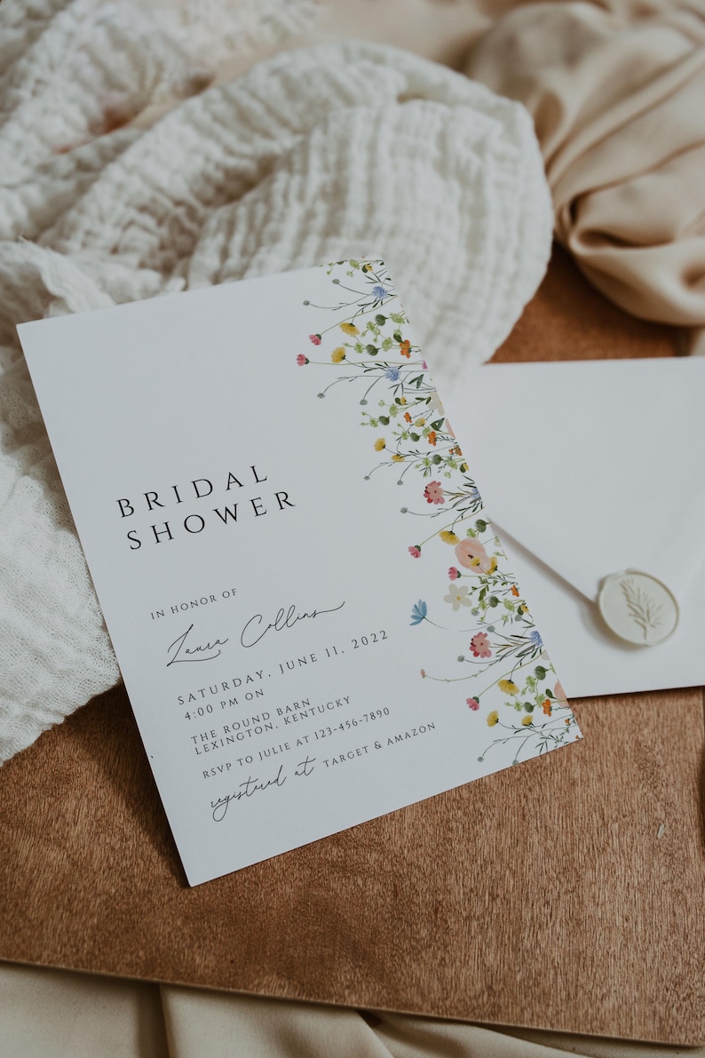 Puede incluir: Una tarjeta blanca con un borde floral y el texto "Bridal Shower" en negro. La tarjeta tambi&eacute;n incluye el texto "En honor de Laura Collins" en cursiva, "S&aacute;bado, 11 de junio de 2022" en negro, "4:00 PM on" en negro, "The Round Barn" en negro, "Lexington, Kentucky" en negro, "RSVP a Julie al 123-456-7890" en negro, y "Registered at Target & Amazon" en negro.