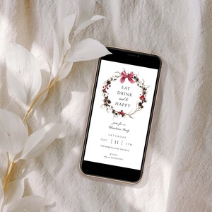 May include: A digital invitation on a smartphone screen with a watercolor wreath of twigs, berries, and cotton. The text reads "Eat Drink and be Happy" and invites guests to a Christmas party on Saturday, December 11th at 3 PM. The address is 120 Maryland Avenue.