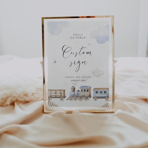May include: A gold-framed sign with a white background and blue watercolor clouds. The text "FULLY EDITABLE Custom sign CREATE AND DESIGN unlimited signs" is printed on the sign. A blue and brown train with three cars is illustrated at the bottom of the sign.