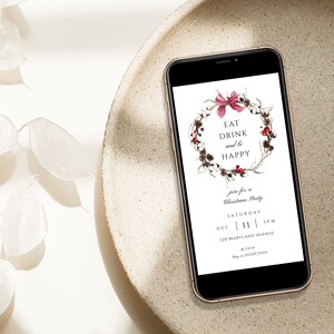 May include: A digital invitation on a smartphone screen for a Christmas party. The invitation features a wreath with red berries and a pink bow, with the text "Eat Drink and be Happy". The invitation includes the date, time, and address of the party.