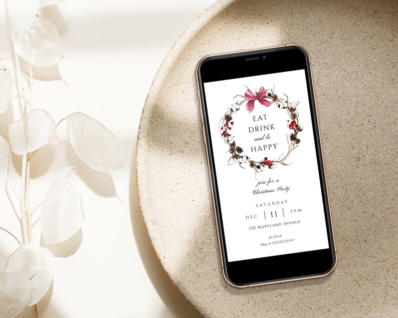 May include: A digital invitation on a smartphone screen for a Christmas party. The invitation features a wreath with red berries and a pink bow, with the text "Eat Drink and be Happy". The invitation includes the date, time, and address of the party.