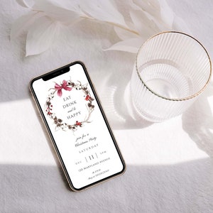 May include: A smartphone displaying a digital invitation for a Christmas party. The invitation features a wreath with red berries and a bow, and the text "Eat Drink and be Happy". The invitation also includes the date, time, and location of the party.