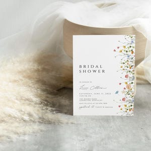 Puede incluir: Una invitaci&oacute;n de ducha nupcial blanca con un borde floral. La invitaci&oacute;n dice "Bridal Shower" en texto negro y "En honor a Laura Collins" en cursiva. La fecha es el s&aacute;bado 11 de junio de 2023.