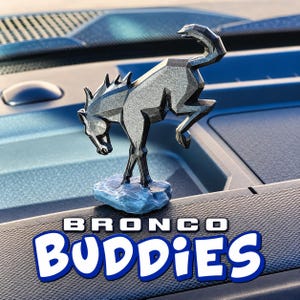 Peut inclure: Une figurine de cheval argentée au style géométrique en position de ruade, montée sur une base bleue texturée. Le texte "BRONCO BUDDIES" est affiché en lettres blanches et bleues au bas de l'image, avec une police grasse et arrondie.