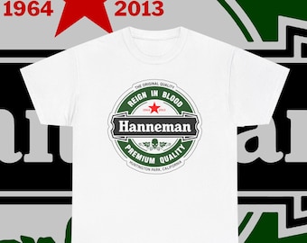 May include: White t-shirt with a circular graphic featuring the text "Hanneman" and "Reign in Blood." The graphic includes a red star, the years 1964 and 2013, and the words "Premium Quality" and "Huntington Park, California."