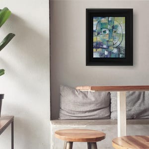 May include: Abstract painting of a face with geometric shapes in shades of green, blue, and yellow. The painting is framed in black and hanging on a gray wall.