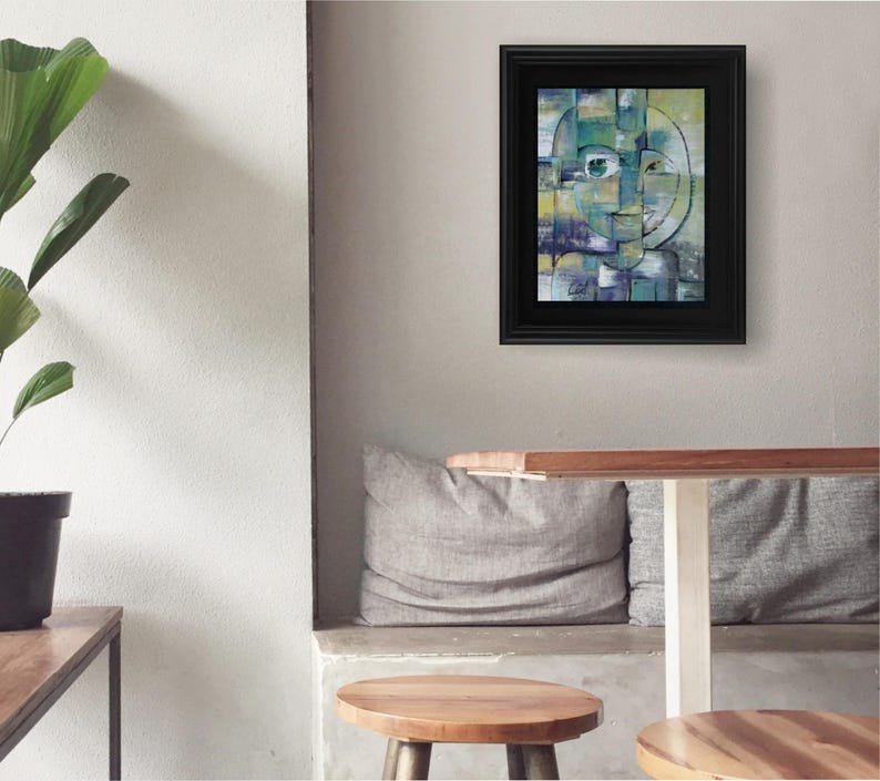 May include: Abstract painting of a face with geometric shapes in shades of green, blue, and yellow. The painting is framed in black and hanging on a gray wall.