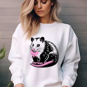 May include: White sweatshirt with a black and white illustration of an opossum wearing a pink bow tie.