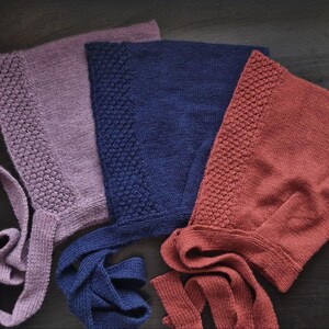 Può includere: Tre berretti di lana con lacci in viola, blu e rosso. I berretti hanno un motivo testurizzato e sono legati con stringhe lunghe.