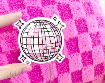 Op de afbeelding: Een roze en witte glitter discobal sticker met sterren op een roze pluche achtergrond. De sticker zit op een zilveren discobal.