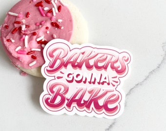 May include: Pink and white cookie with red and white sprinkles. A pink and white sticker with the text "Bakers Gonna Bake" in a pink and white gradient.