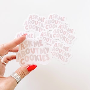 May include: A stack of pink and white stickers with the text "Ask Me About My Cookies" on them.
