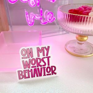 Può includere: Sticker rosa e bianco con il testo "ON MY WORST BEHAVIOR" in un font sfumato rosa e bianco.