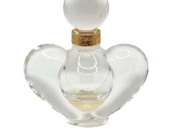 Può includere: Un flacone di profumo in vetro trasparente con una base a forma di cuore e un tappo rotondo in vetro trasparente. Il flacone ha una fascia dorata intorno al collo.