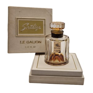 May include: A vintage perfume bottle with a clear glass body and a gold-coloured cap. The bottle is labelled "Sortilege Le Galion Paris" and is sitting on a white box with a gold trim. The box is labelled "Sortilege Le Galion 1/2 FL OZ".