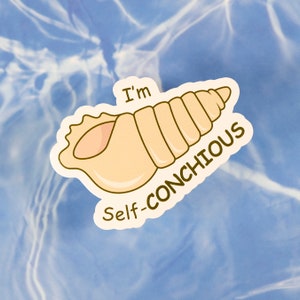 Könnte beinhalten: Ein Aufkleber mit einer Cartoon-Muschel in Beige und Rosa, mit dem Text "I'm Self-CONCHIOUS" in Braun. Der Aufkleber befindet sich auf einem blauen Hintergrund mit einem wasserähnlichen Muster.