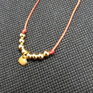 Puede incluir: Un brazalete de cuerda roja con cuentas doradas y un dije en forma de corazón.