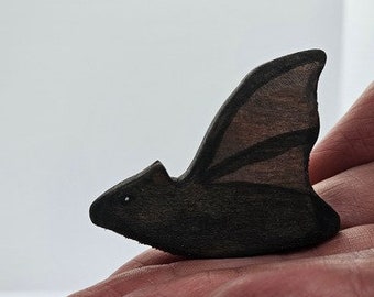 May include: A black wooden bat figurine with wings outstretched. The bat is sitting on a hand.