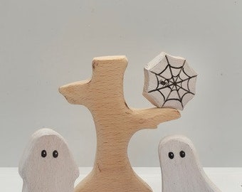 May include: A wooden Halloween set with two white ghost figurines and a tree with a spider web. The ghosts have black eyes and the spider web is black on a white background.