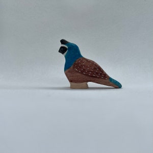May include: A wooden bird figurine with a blue head and chest, brown body with white dots, and a light brown base. The bird has a black crest and a blue tail. The figurine is hand-painted and stands on a white surface.