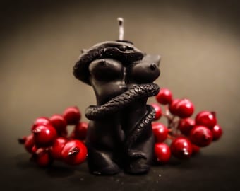 May include: A black candle shaped like a torso with a snake wrapped around it. The candle is sitting on a bed of red berries.