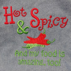 Puede incluir: Diseño bordado sobre un fondo de tela gris. El texto dice "Hot & Spicy And my food is amazing, too!" con bordado rojo y verde. El diseño incluye dos chiles rojos y verdes.