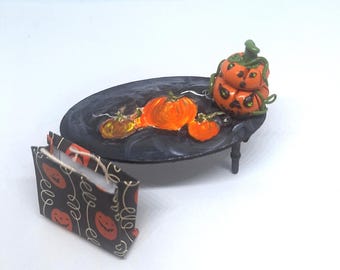 May include: A miniature Halloween scene featuring a black table with orange pumpkins and a stacked pumpkin decoration. A small shopping bag with a pumpkin pattern sits nearby. The scene is set against a white background.