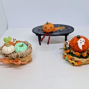 May include: A Halloween display with miniature pumpkins and ghosts. One pumpkin sits on a small table, while others are arranged in woven baskets. The pumpkins are orange, white, and green, with ghost figures.