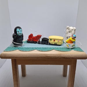 Puede incluir: Una pequeña mesa de madera con una superficie estampada en color turquesa exhibe pequeñas figuras de cerámica. Las figuras incluyen un gorila, un tren rojo, un vagón amarillo y negro, un oso blanco y un payaso.