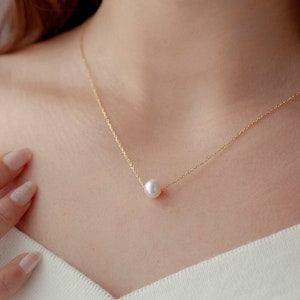May include: A delicate gold chain necklace with a single white pearl pendant.