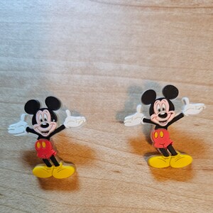 May include: Two plastic Mickey Mouse figures with outstretched arms and yellow shoes. The figures are red, black, and white.