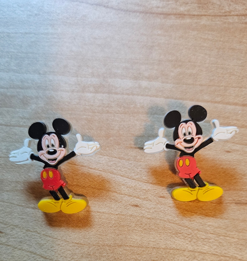 May include: Two plastic Mickey Mouse figures with outstretched arms and yellow shoes. The figures are red, black, and white.