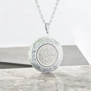 May include: Silver-toned round locket pendant with a detailed floral design. The locket features a coin with the text "SIX PENCE 1966" at the center. The pendant hangs from a delicate silver chain, creating a classic and elegant accessory.