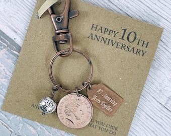 Puede incluir: Un llavero de tono cobre con un dije que dice "10 Amazing Years Together" y una moneda británica de un penique. El llavero también tiene un dije de corazón y una etiqueta que dice "Happy 10th Anniversary".
